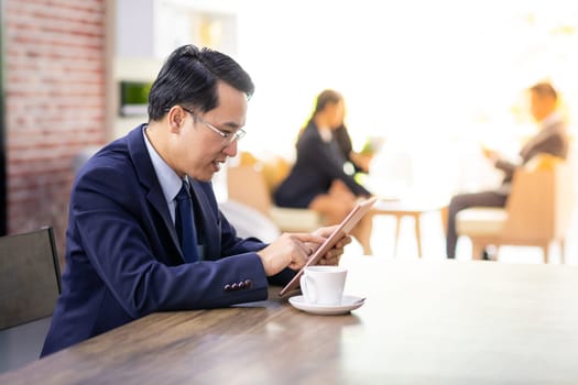 Portrait of Businessman working in cafe with smart phone and tablet with business team in background using for coporate background work