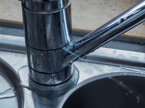 Close-up of a leaking faucet with jetting out the jet of water on a sink at the window.
