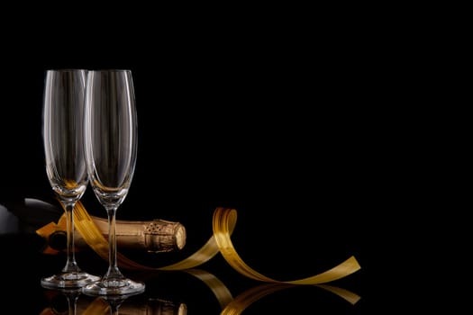 Two wineglasses with champange, bottle and serpentine on a dark background with ligth and reflection. Copy space. Christmas and New Year background