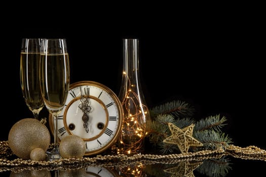 Two wineglasses with champange, bottle, gift box, clock and christmas ornament on a black background with reflection. Copy space. Christmas and New Year background