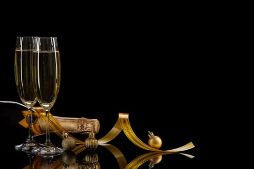 Two wineglasses with champange, bottle and serpentine on a black background with reflection. Copy space. Christmas and New Year background