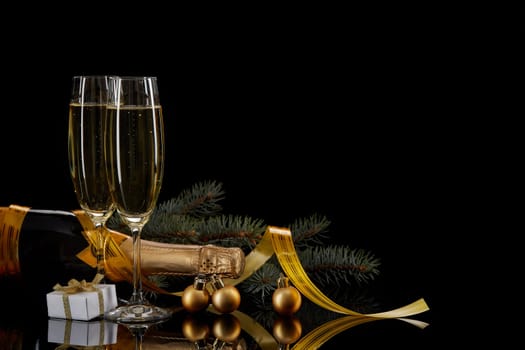 Two wineglasses with champange, bottle, gift box and serpentine on a black background with reflection. Copy space. Christmas and New Year background