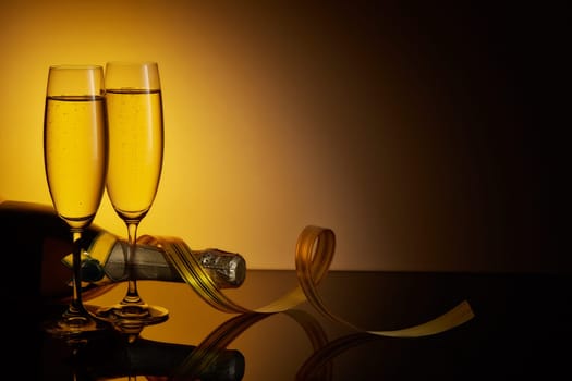 Two wineglasses with champange, bottle and serpentine on a dark background with ligth and reflection. Copy space. Christmas and New Year background