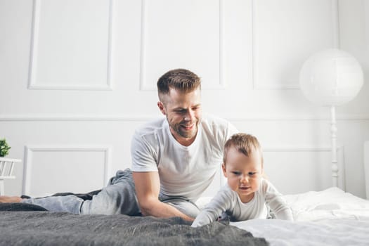 Happy father with his one year old son playing at home on the bed
