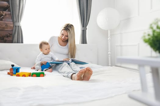 Child education. Happy mother with her toddler sitting on the bed and reading a book together