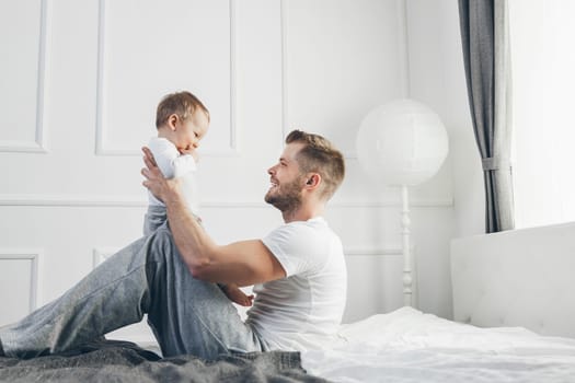 Happy father with his one year old son playing at home on the bed