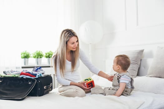 Travelling with kids. Happy mother with her child packing clothes for their holiday
