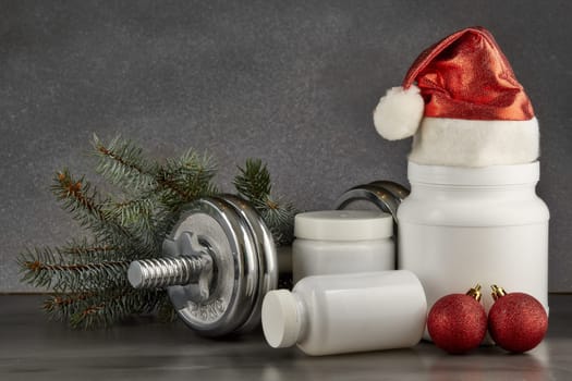 Sports nutrition (supplements), dumbbells, fir tree branches and christmas ormament on a dark background. Horizontal view. New Year and Christmas. Fitness. Healthy lifestyle.