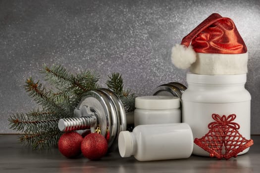 Sports nutrition (supplements), dumbbells, fir tree branches and christmas ormament on a dark background. Horizontal view. New Year and Christmas. Fitness. Healthy lifestyle.