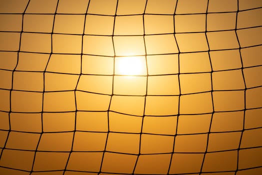 Football goal net at sunset. Meshed pattern with sun and sunset sky in background.