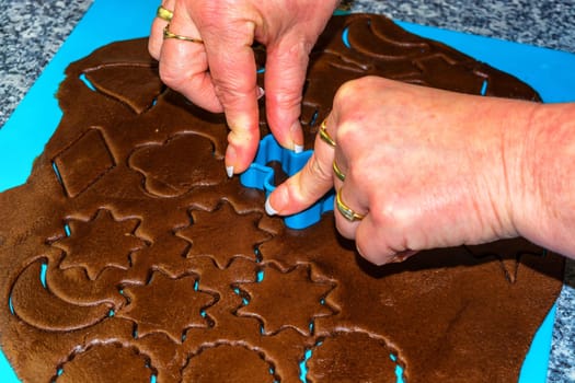 Female hand making the traditional Christmas cookies. Raw dough is being punched out for the holiday cookies on a blue underlay. Preparing gingerbread cookies.