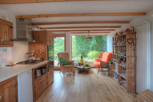 A wide view shot of a simplistic kitchen, to the left is an oven and stoves and to the right is shelves with kitchen supplies.