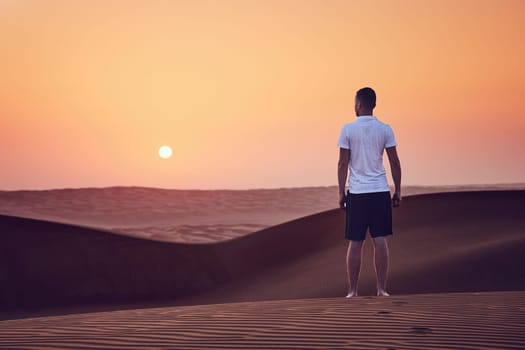 Sunrise in desert. Lonely man walking on sand dune. Wahiba Sands in Oman.