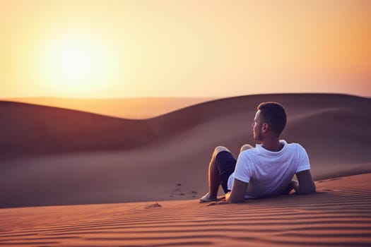 Idyllic sunrise in desert. Young man contemplation on sand dune. Wahiba Sands in Oman.