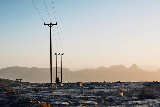 Pylons with power lines in mountains at colorful sunset, Oman