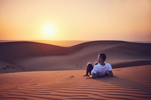 Idyllic sunrise in desert. Young man contemplation on sand dune. Wahiba Sands in Oman.