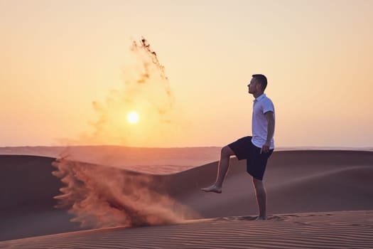 Happy man kicking sand and having fun in desert at sunrise. Wahiba Sands in Oman
