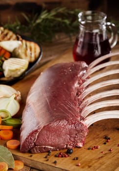 A gourmet, uncooked rack of ribs on a timber chopping board with condiments, herbs and vegetables.