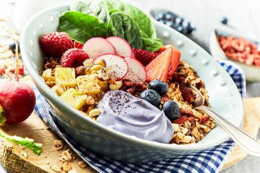 Bawl of muesli with berries in rustic style, served on checked blue fabric napkin over wooden chopping board. Viewed in close-up, from the side