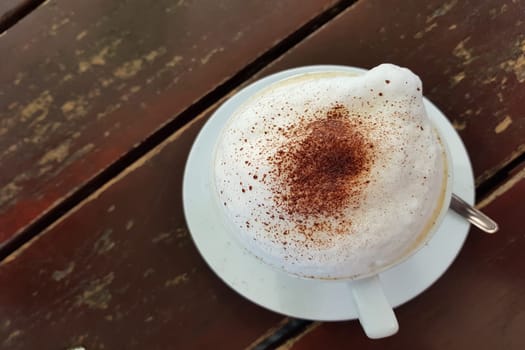 Closeup on a plain white coffee cup with milk foam after latte style on brown wooden table top in a cafe.