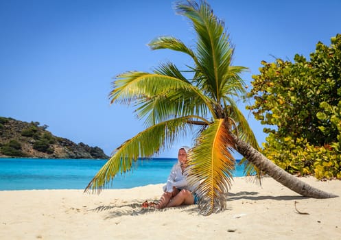 Woman is resting in shade of a palm tree on a beach in British Virgin Islands