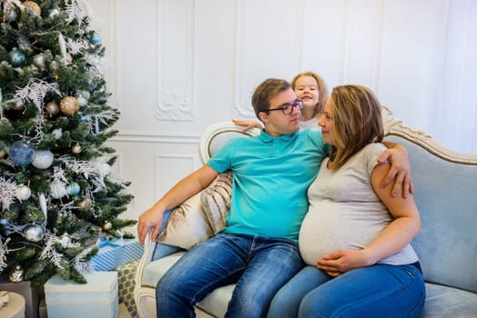 Family portrait near christmas tree. Pregnant woman. Funny daughter on the background.