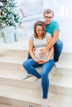 Family portrait near christmas tree. People sitting on the staircase. Pregnant woman