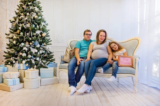 Family portrait near christmas tree. Pregnant woman
