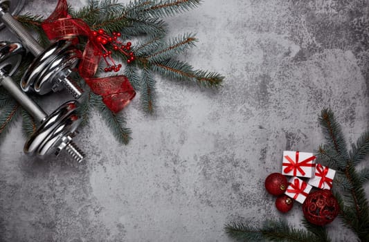 Dumbbells, boxing gloves, fir tree branches and Christmas decorations on a gray background.Top view with copy space. New Year and Christmas. Fitness, sport and healthy lifestyle concept.