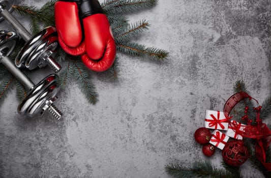 Dumbbells, boxing gloves, fir tree branches and Christmas decorations on a gray background.Top view with copy space. New Year and Christmas. Fitness, sport and healthy lifestyle concept.