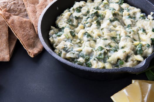 Pan with fresh vegan spinach artichoke dip and whole wheat pita bread.