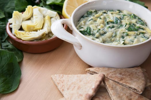 Bowl of vegan spinach artichoke dip with pita and ingredients.