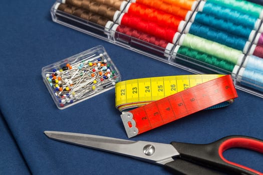 sewing equipment blue fabric scissors box with colorful cottons measuring tape and pin needles on blue fabric