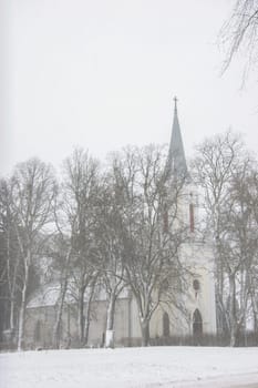 Church in snowfall. Winter in Barbele, Latvia. Church covered in snow. Winter landscape with snow covered church and trees...