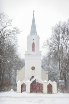 Church in snowfall. Winter in Barbele, Latvia. Church covered in snow. Winter landscape with snow covered church and trees.....