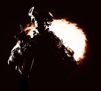 High contrast portrait of confident special operations forces soldier, armed and equipped, valiantly standing on black background with ball of fire. Heroic, brave veteran of war or military conflict