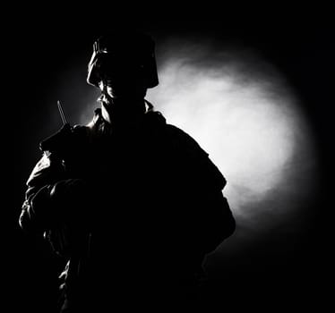 Silhouette photo of army soldier, modern combatant, military conflict participant standing in combat uniform with fiery spot on black background. Fire of war, ashes of battle, nuclear fire concept