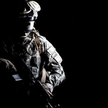 Armed army soldier in camouflage uniform, with hidden face, sneaking in dark during combat, counter terrorist raid. Secret military operation, stealth mission under cover of darkness, night patrol