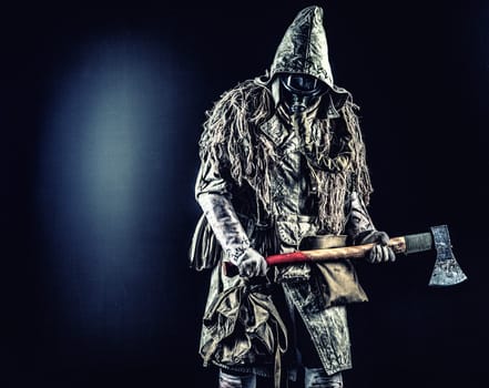 Post apocalyptic survivor, radioactive zone stalker, crazy serial killer or maniac in gas mask and tattered clothes decorated with runes, threatening with raised ax isolated on black studio shoot