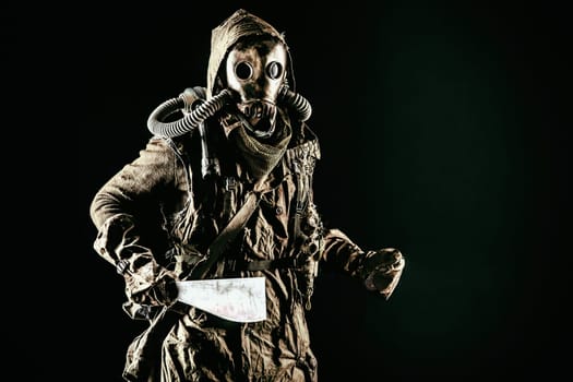Low key portrait of post apocalyptic creature, living in catacombs mutant, survived in nuclear disaster human in ragged cloth and gas mask, armed with handmade cold weapon isolated on black background