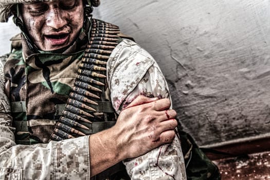 Army soldier, commando fighter, marine machine gunner wounded in shoulder, clamping wound with healthy hand. Infantryman with gunshot wound in upper limb, trying stop bleeding, waiting for medical aid