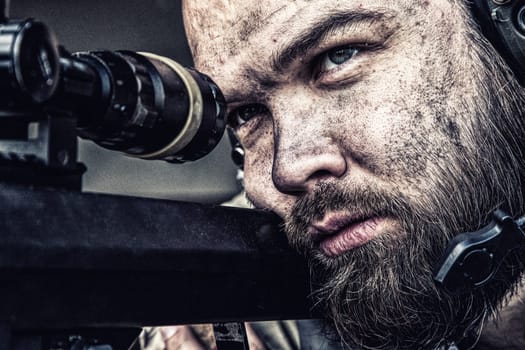 Army sniper with bearded, dirty face aiming with optical telescopic sight on sniper rifle, observing battlefield from ambush and searching targets to shoot, shooting on long range distances, close up