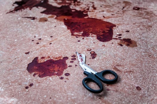 Trauma shears or bandage scissors lying on floor with stains of human blood around. Blood loss and bleeding stop, emergency medical aid for gunshot wounds, tactical combat casualty care on battlefield