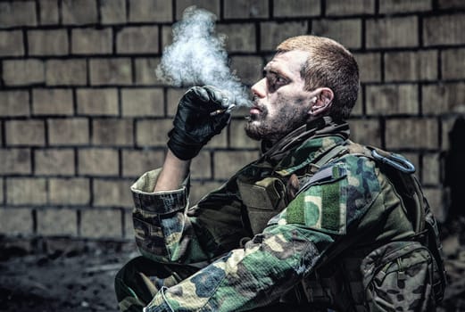 Special forces soldier after the fight sitting in ruined building smoking cigarette staring at the camera