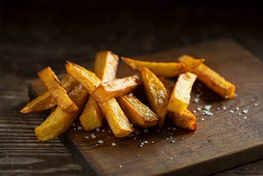 Delicious salty french fries on wooden table and dark background