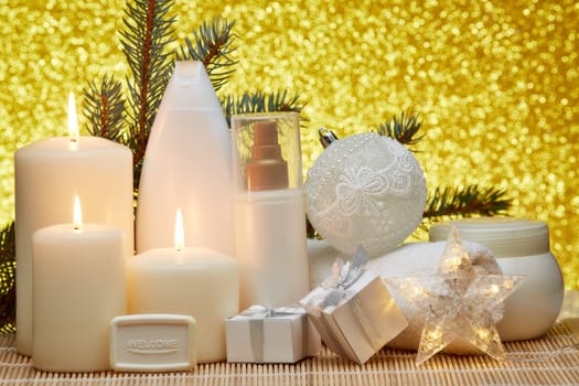 Spa still life with cosmetic creams, candles, fir branches, gift boxes and Christmas ornaments on a gold background. Healthy lifestyle, body care, Spa treatment and relaxation concept.