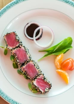 Seared tuna with sesame seeds with green salad on white plate