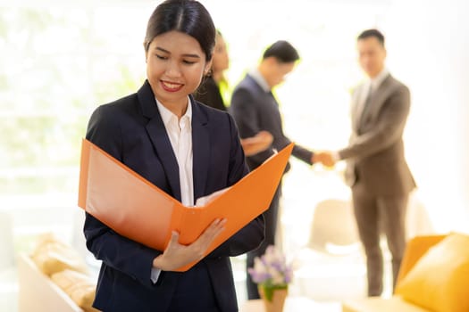 Portrait of Asian Businesswoman hold working file with business team in background using for coporate background work