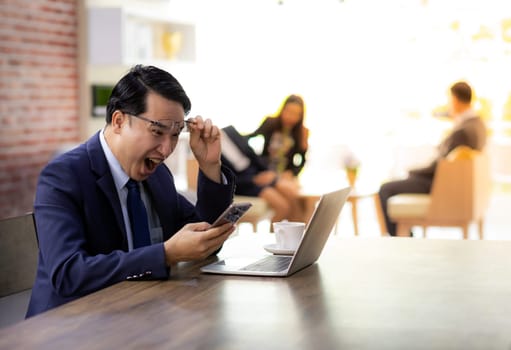 Portrait of Asian Businessman celebrate and glad for his success in cafe using smart phone and laptop with business team in background using for coporate background work