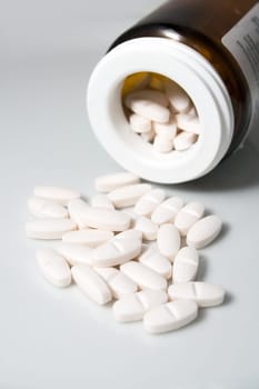 white pilled pills from a bottle on white background